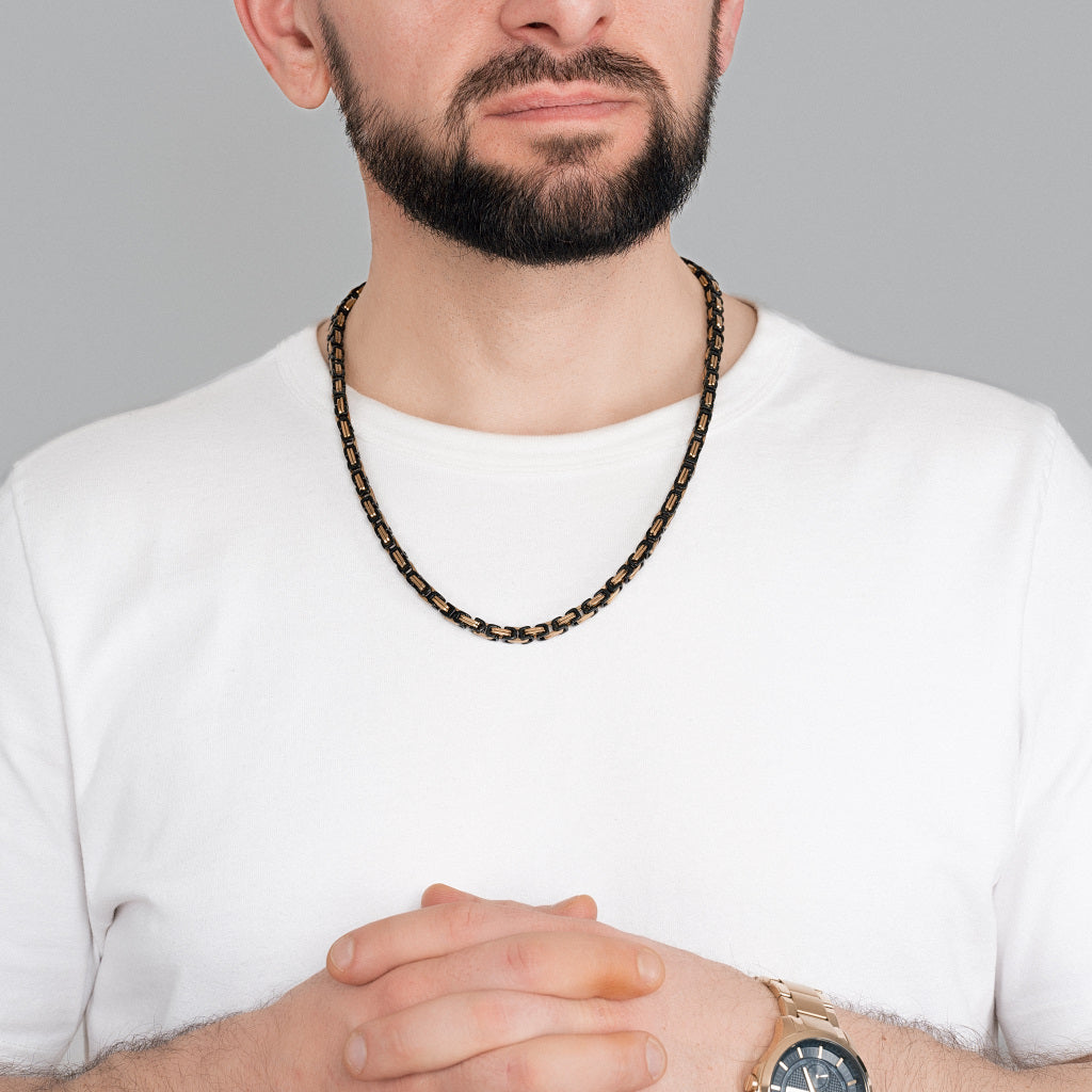 A bearded man in white t-shirt wearing 2 tone Gold Black Byzantine Box link Chain 5mm, 24 inches with a gold watch to perfectly match the accessories