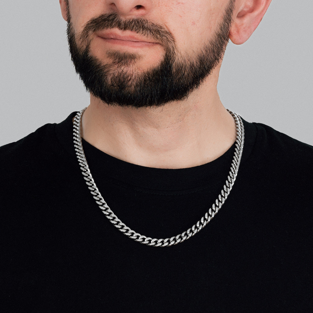 A bearded brutal male model in black t-shirt wearing Silver Miami Cuban Chain 8 mm. Close-up detailed view of Miami Cuban Chain.