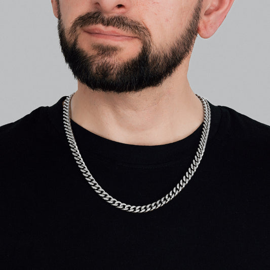 A bearded brutal male model in black t-shirt wearing Silver Miami Cuban Chain 8 mm. Close-up detailed view of Miami Cuban Chain.