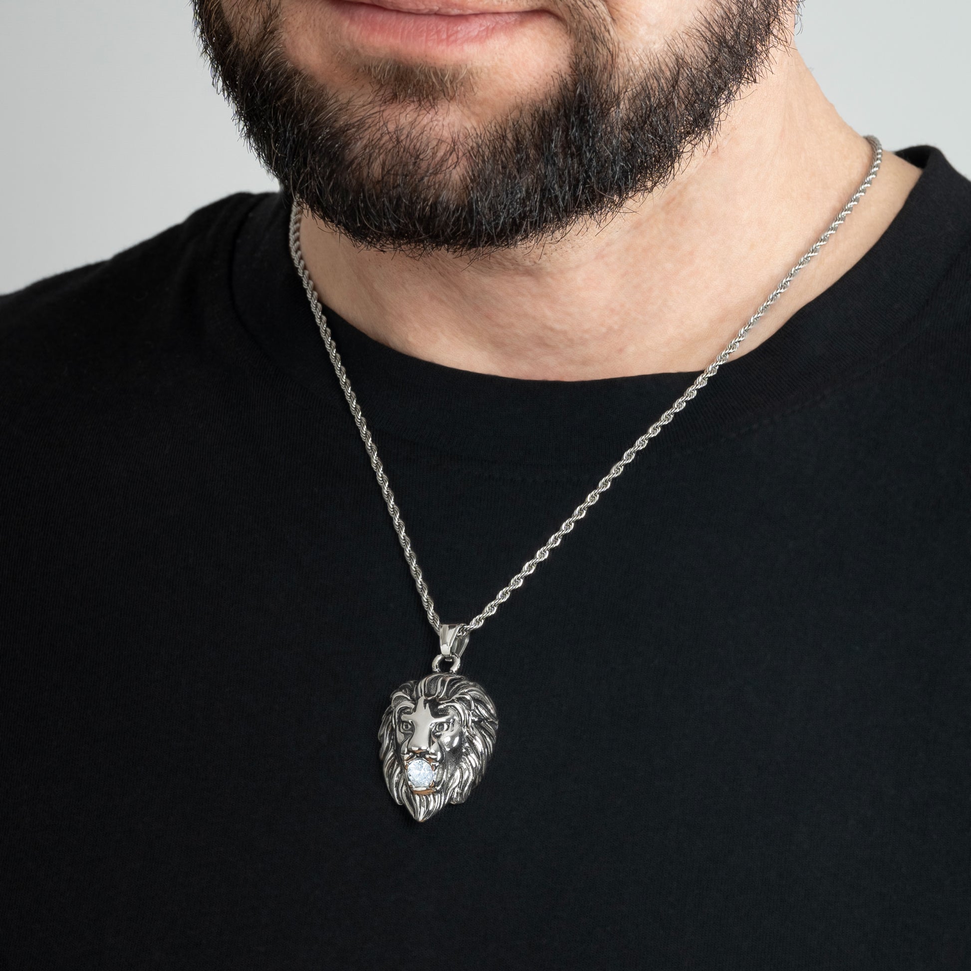 A male model in a black t-shirt wearing a Lion Head Crystal Silver Pendant with a Silver Rope chain 22 inches. Close-up image of the non-tarnish trending silver necklace with Cubic Zirconia insert in Lion's mouth.