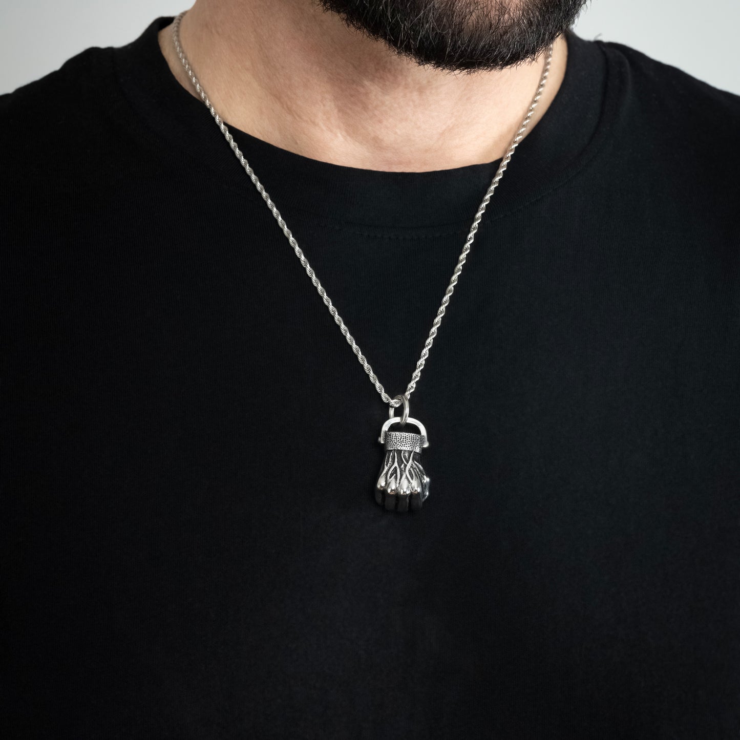 A male model in a black t-shirt wearing a Fist Silver Pendant with a Silver Rope chain 22 inches. Close-up image of the non-tarnish, waterproof trending clenched fist necklace.