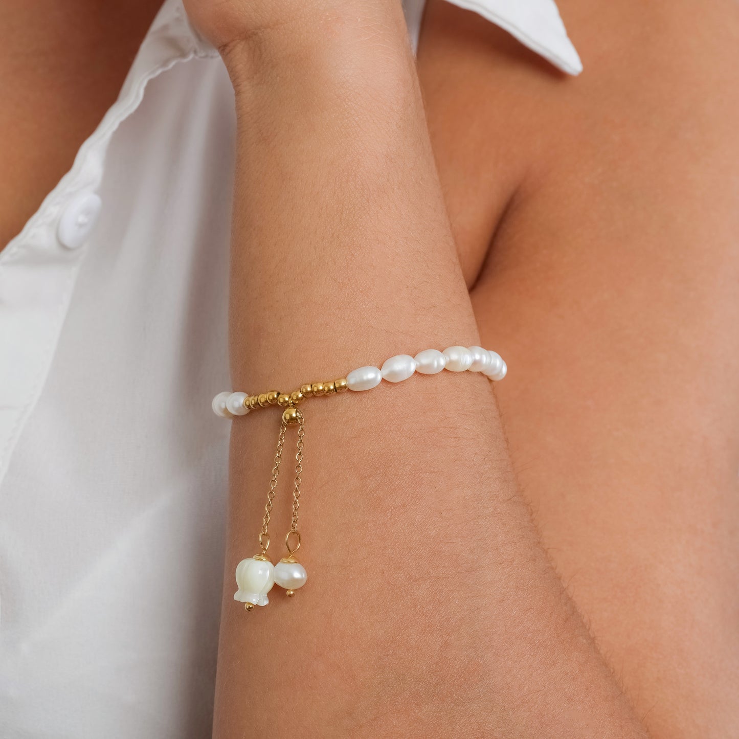 A model in a white sleeveless top wearing Lily of the Valley Pearl bracelet on her wrist. Close-up image of the bracelet.