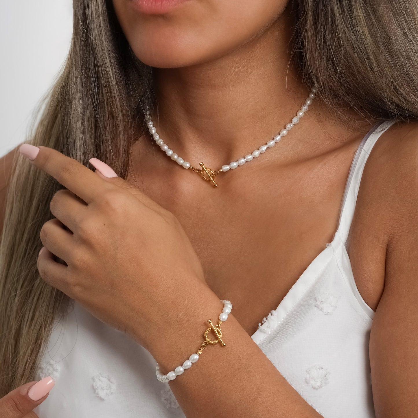 A model in a white dress wearing Toggle Clasp Pearl Choker Necklace paired with Toggle Clasp Pearl Bracelet on her wrist