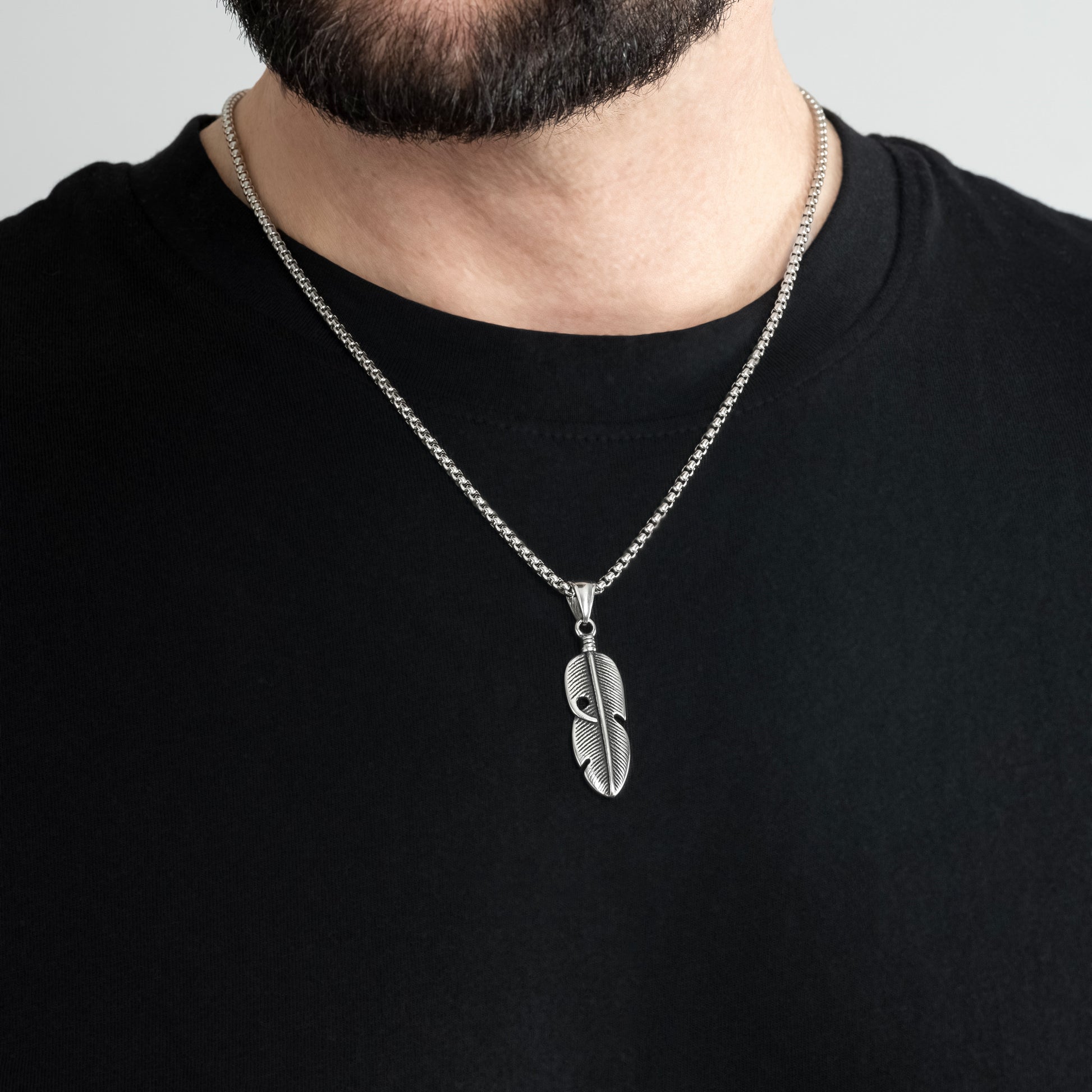 A male model in a black t-shirt wearing a Feather Leaf Silver Pendant with a 3mm Silver Round Box link chain 22 inches. Close-up image of the non-tarnish, sweatproof trending men's necklace talisman..