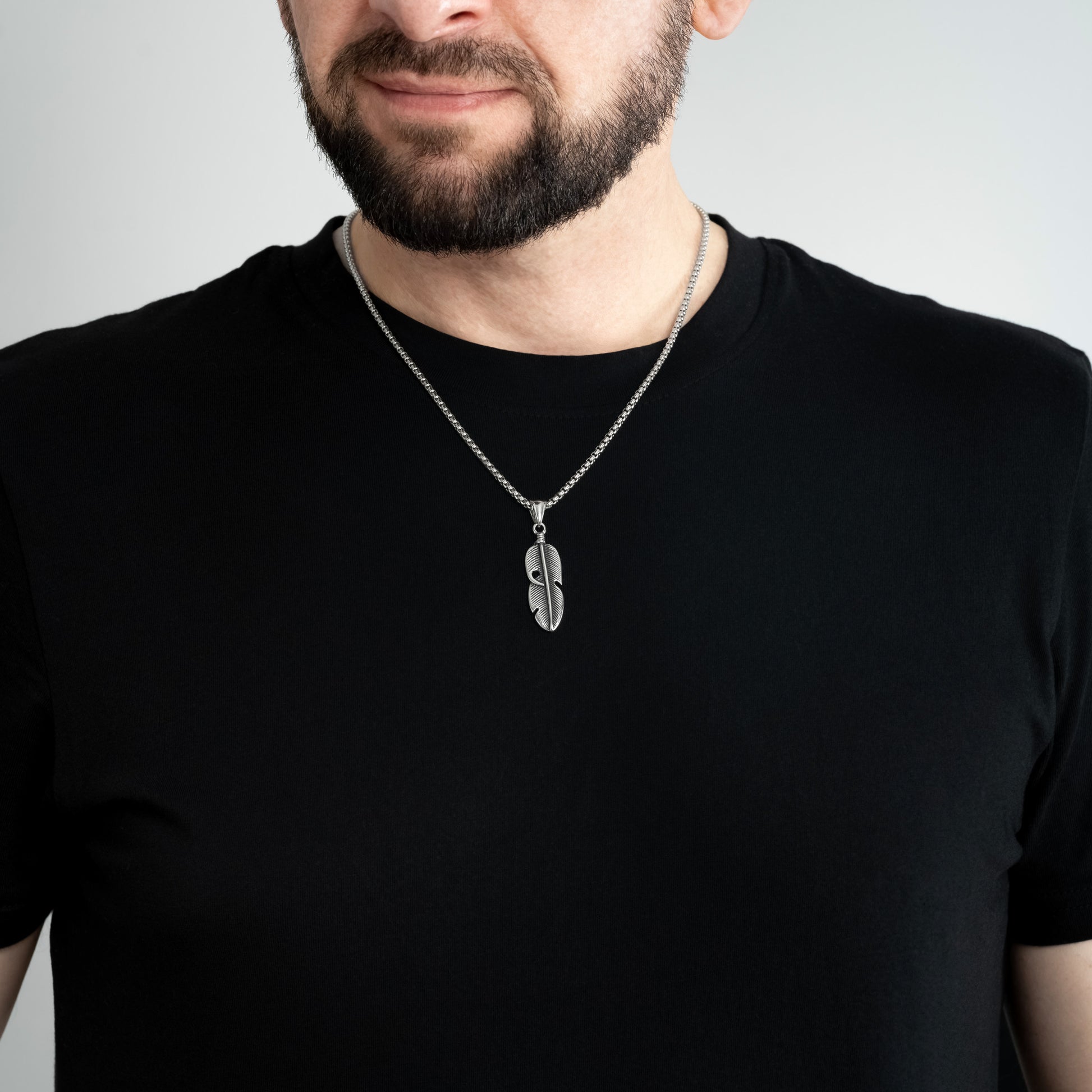 A male model in a black t-shirt wearing a Feather Leaf Silver Pendant with a 3mm Silver Box link chain 22 inches.