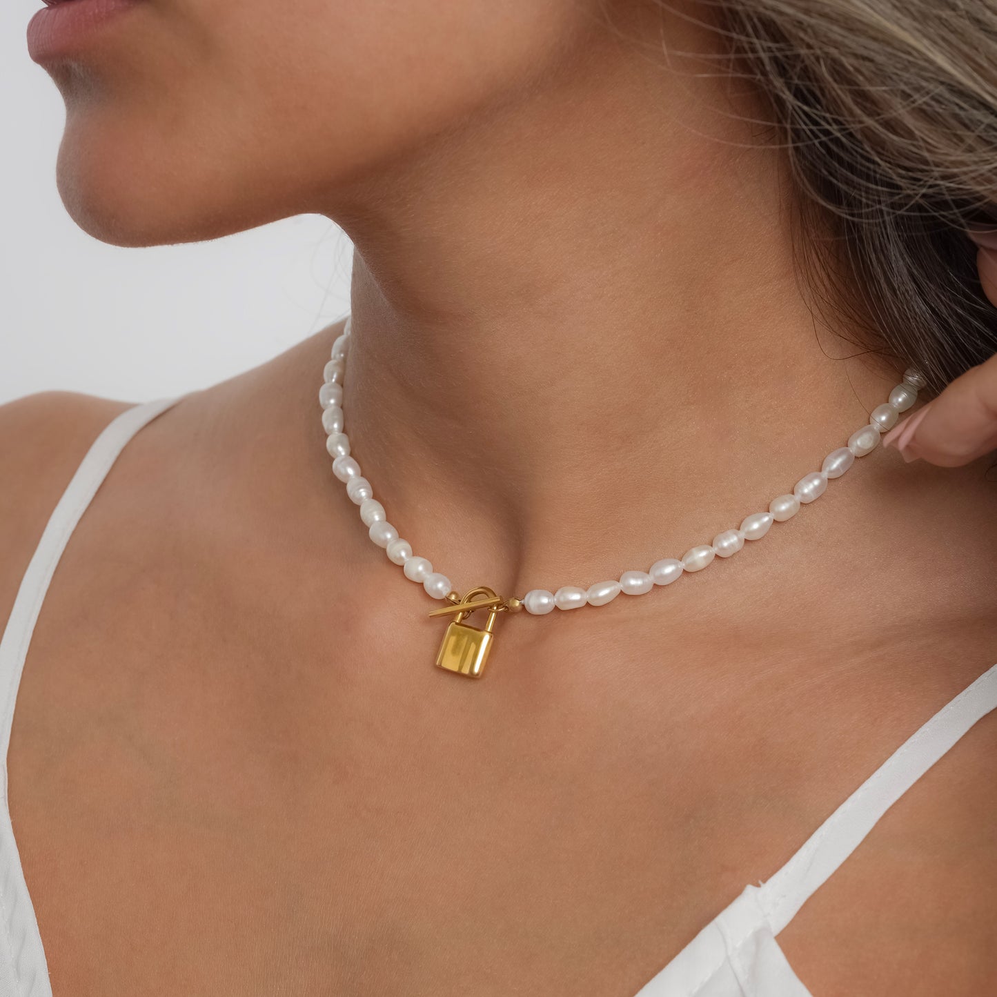 A model in a white dress wearing Padlock Pearl Necklace. Close-up image of the necklace.