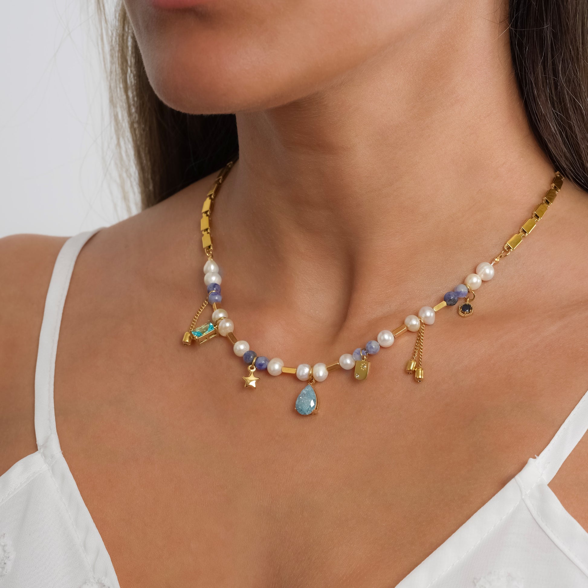 A model in a white dress wearing Crystal Charm Pearl Gold Necklace. Close-up image of the necklace.