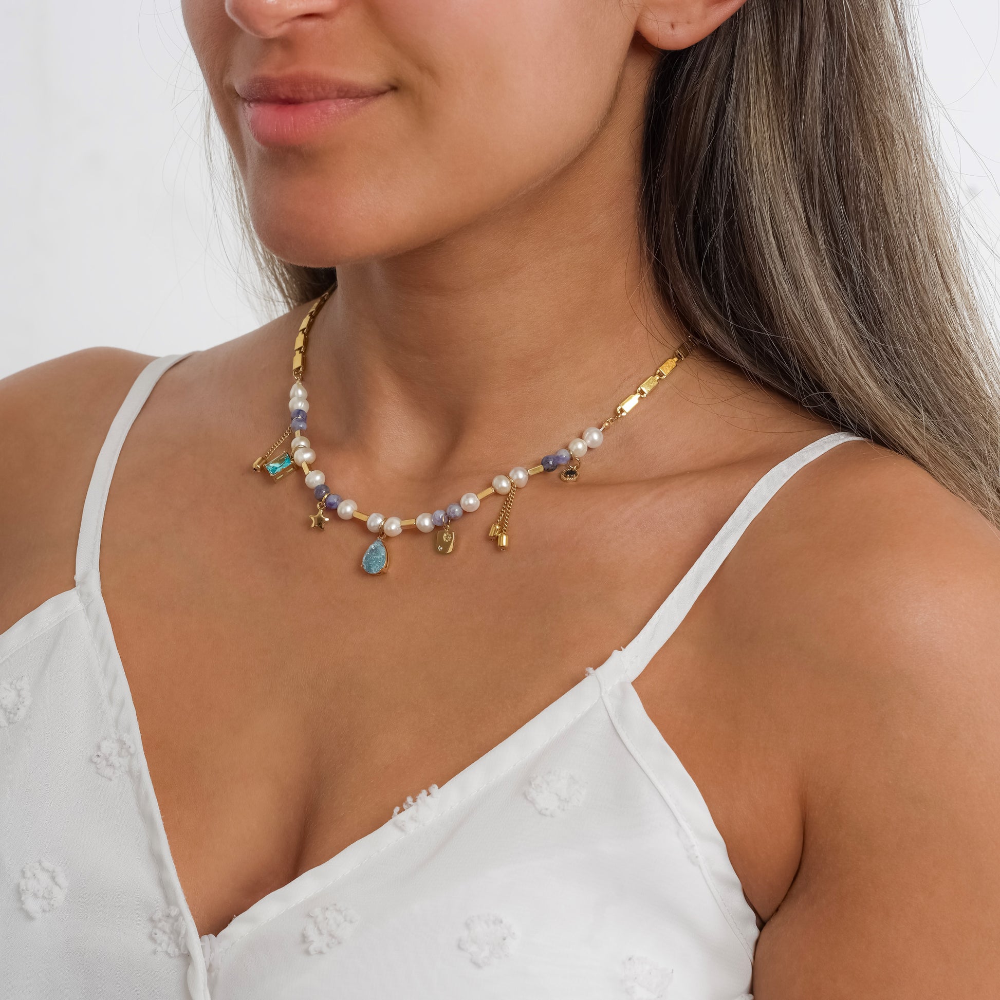 A model in a white dress wearing Crystal Charm Pearl Gold Necklace.