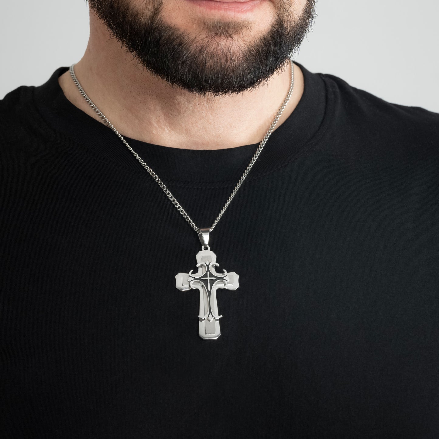 A male model in a black t-shirt wearing a Trinity Cross Silver Pendant with a 3mm Silver Micro Cuban chain 22 inches. Close-up image of the non-tarnish religious men's cross necklace.