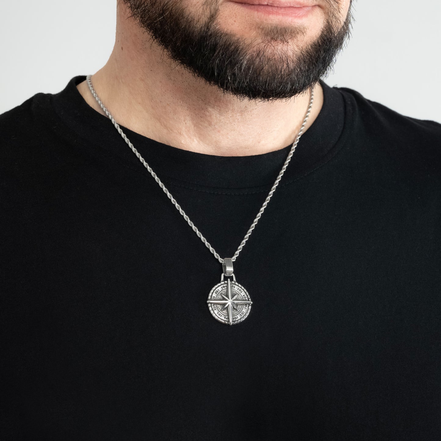 A male model in a black t-shirt wearing a Compass North Star Silver Pendant with a Silver Rope chain 22 inches. Close-up image of the trending non-tarnish necklace.