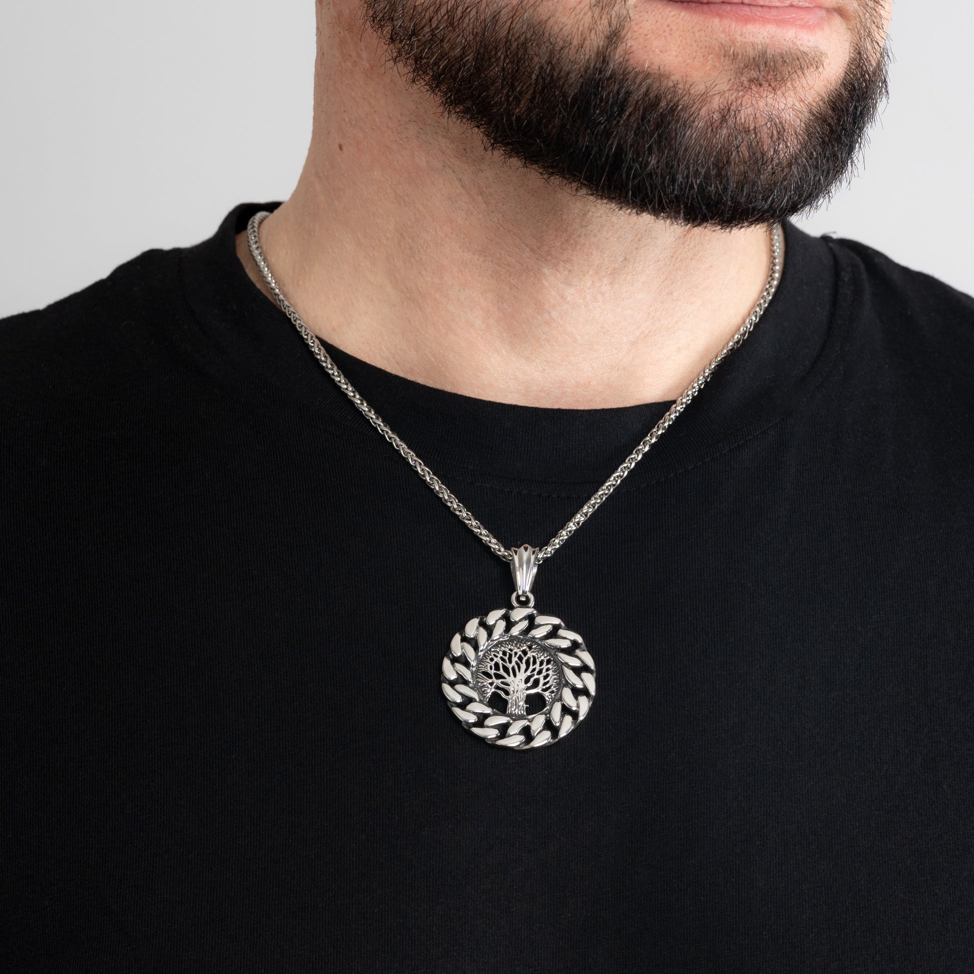 A male model in a black t-shirt wearing a Vintage Tree of Life Silver Pendant with a 3mm Silver Spiga chain 20 inches. Close-up image of the non-tarnish, waterproof and meaningful men's necklace talisman.