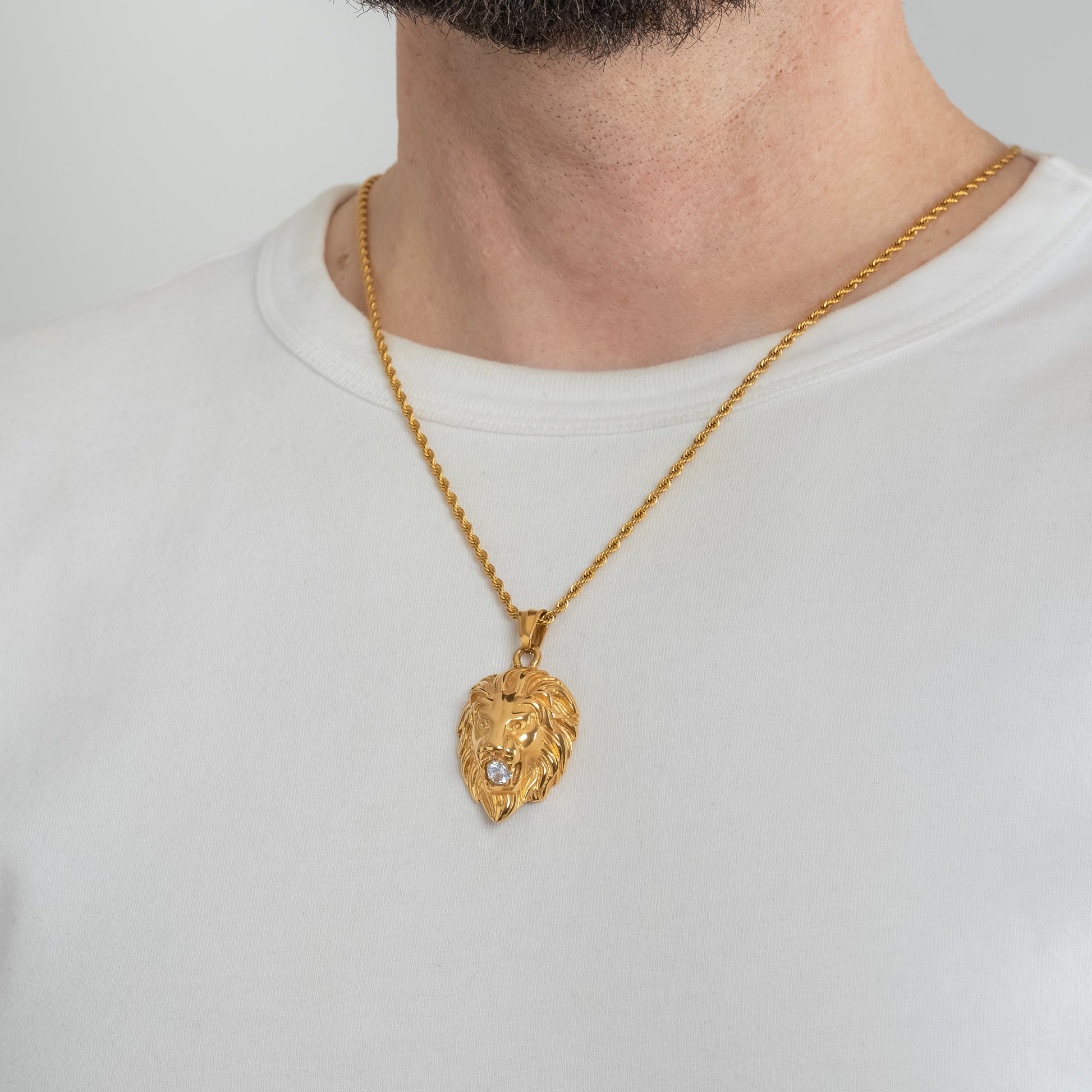 A male model in a white t-shirt wearing a Lion Head Crystal Gold Pendant with a Gold Rope chain 22 inches. Close-up image of the non-tarnish trending necklace with Cubic Zirconia stone insert in Lion's mouth.