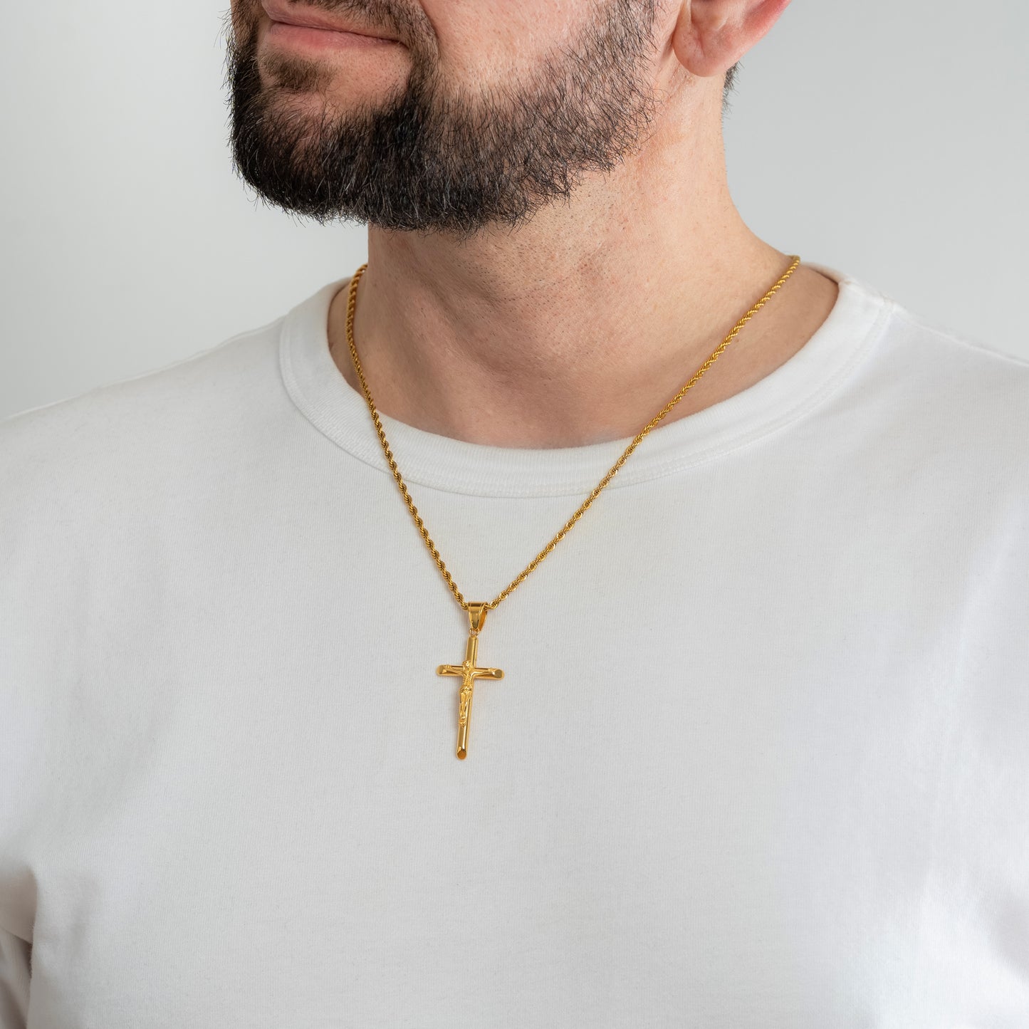 A male model in a white t-shirt wearing a Jesus Crucifix Minimalist Cross Gold Pendant with a 3mm Gold Rope chain 22 inches.