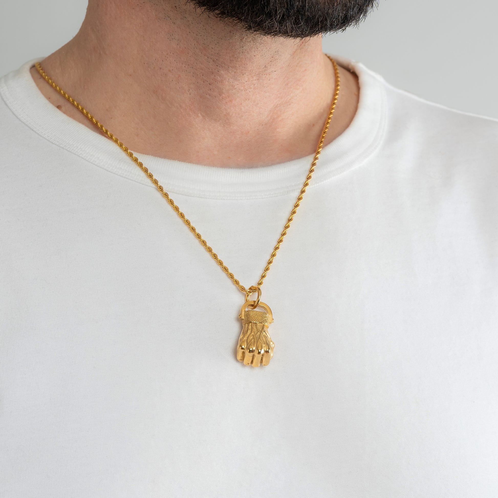 A male model in a white t-shirt wearing a Fist Gold Pendant with a Gold Rope chain 22 inches. Close-up image of the non-tarnish powerful men's necklace.