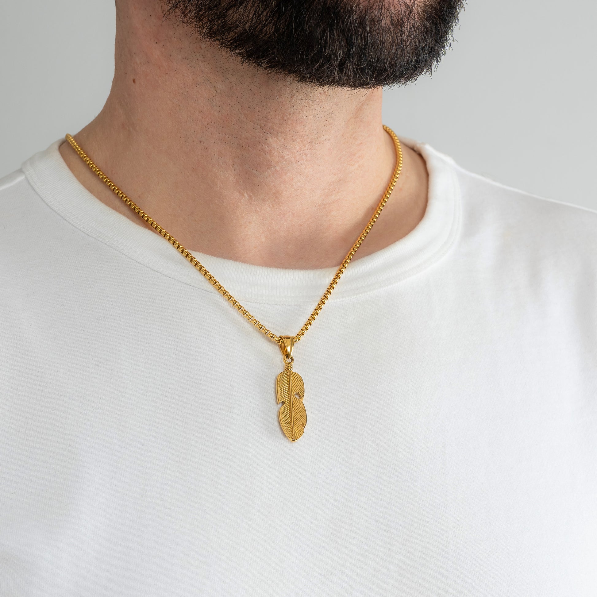 A male model in a white t-shirt wearing a Feather Leaf Gold Pendant with a 3mm Gold Box Link chain 20 inches. Close-up image of the non-tarnish, waterproof trending necklace.