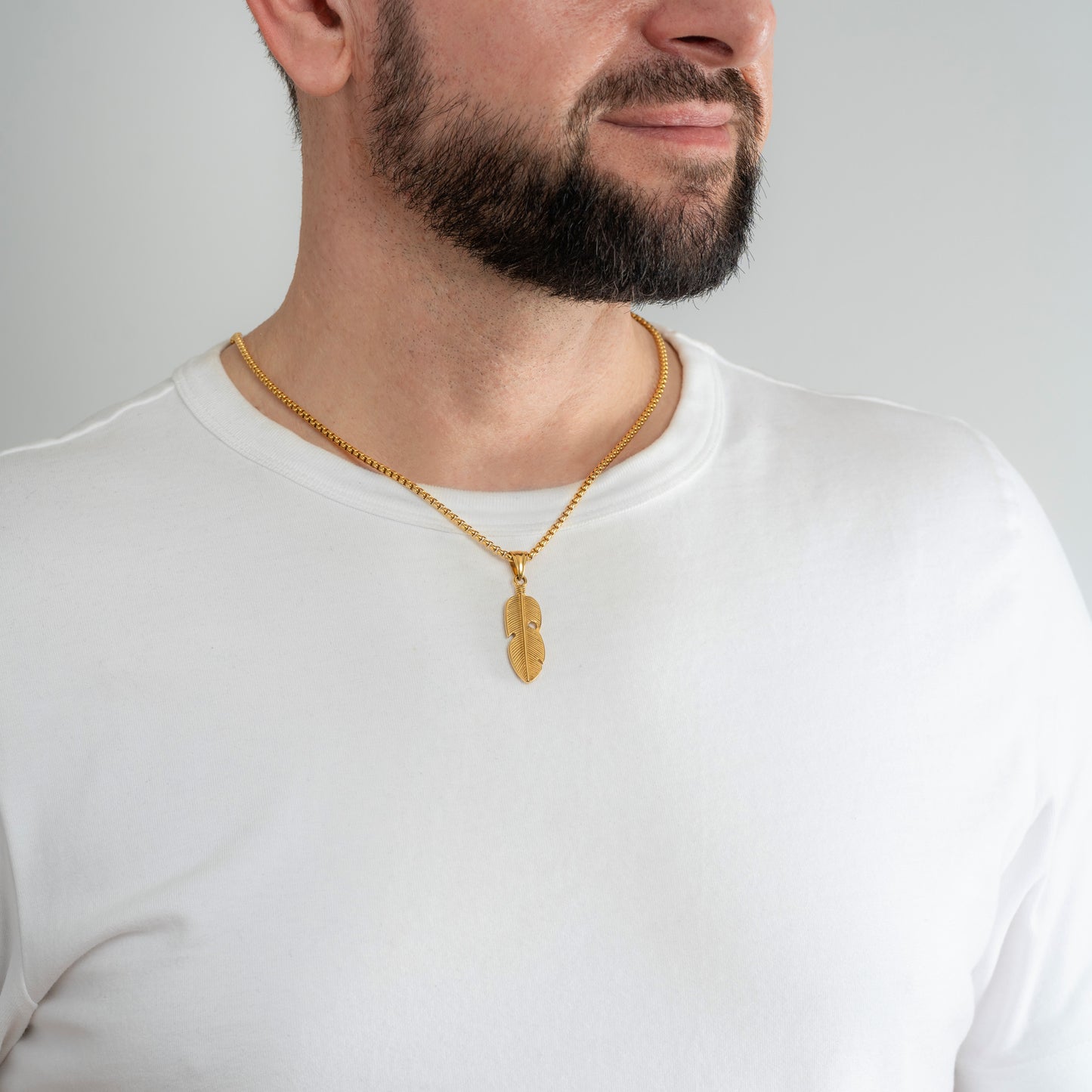 A male model in a white t-shirt wearing a Feather Leaf Gold Pendant with a 3mm Gold Box Link chain 20 inches.