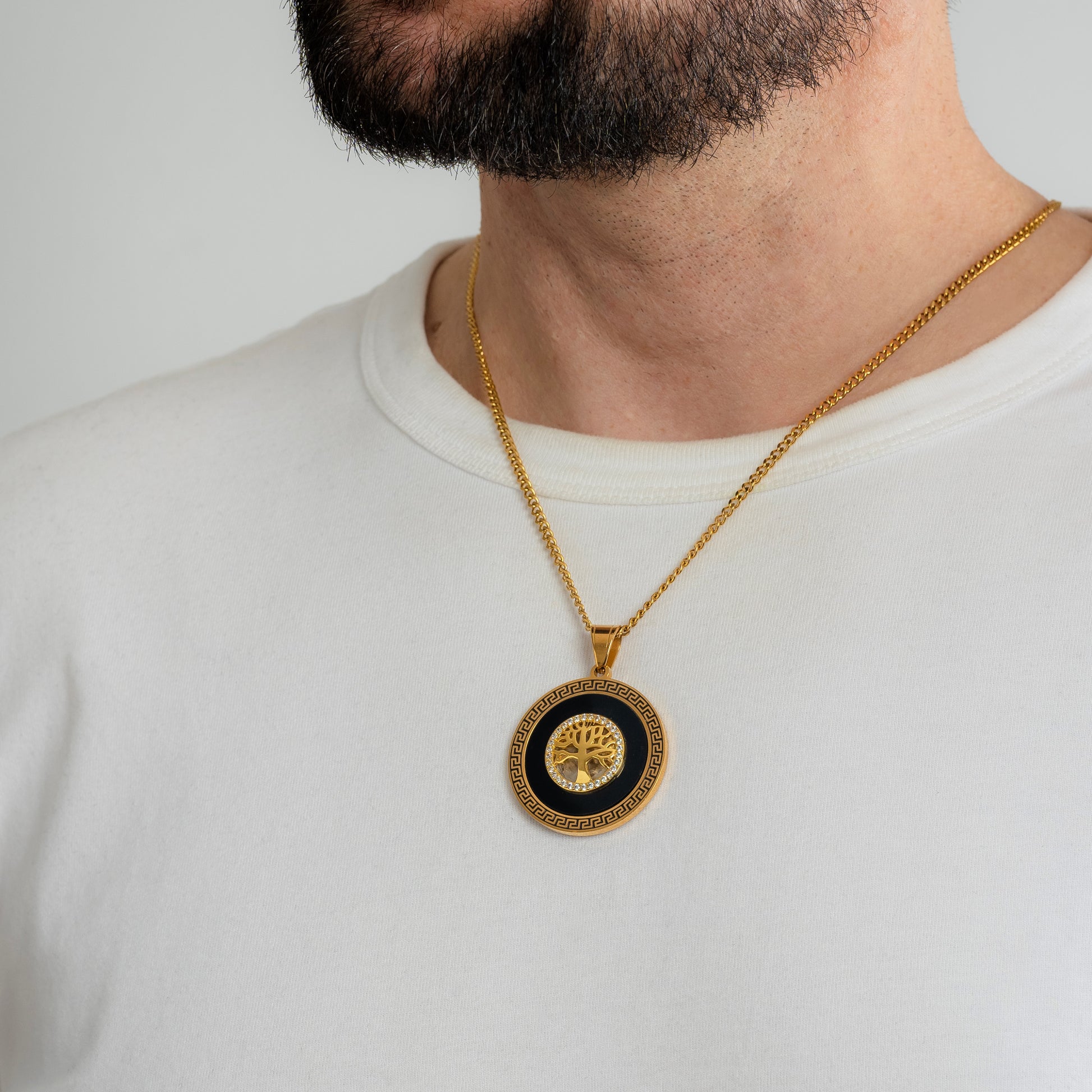 A male model in a white t-shirt wearing an Iced Tree of Life Gold Pendant with a 3mm Micro Cuban chain 22 inches. Close-up image of the non-tarnish, waterproof trending men's necklace with Cubic Zirconia inlays.