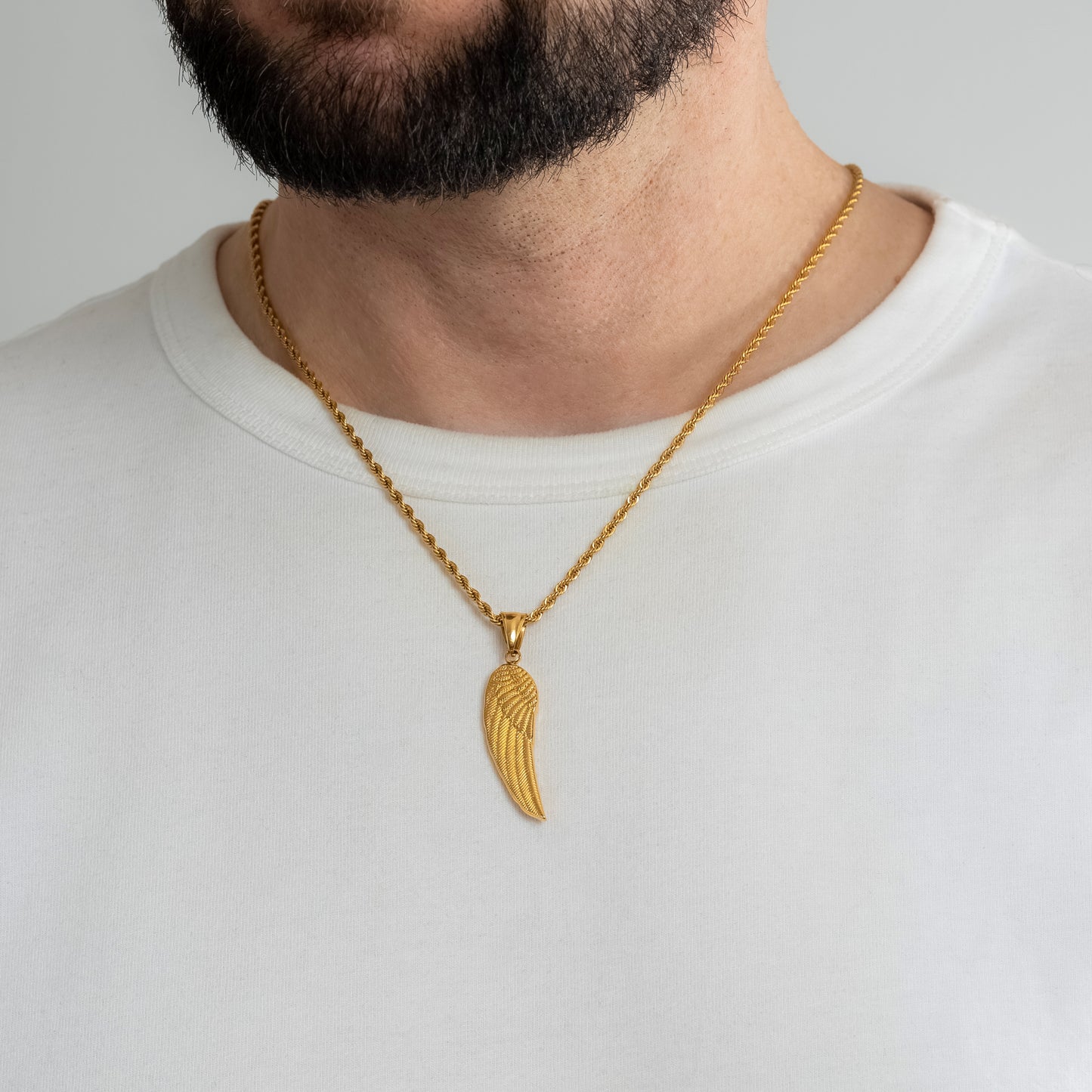 A male model in a white t-shirt wearing an Angel Wing Gold Pendant with a 3mm Gold Rope chain 22 inches. Close-up image of the non-tarnish, waterproof trending men's jewellery.
