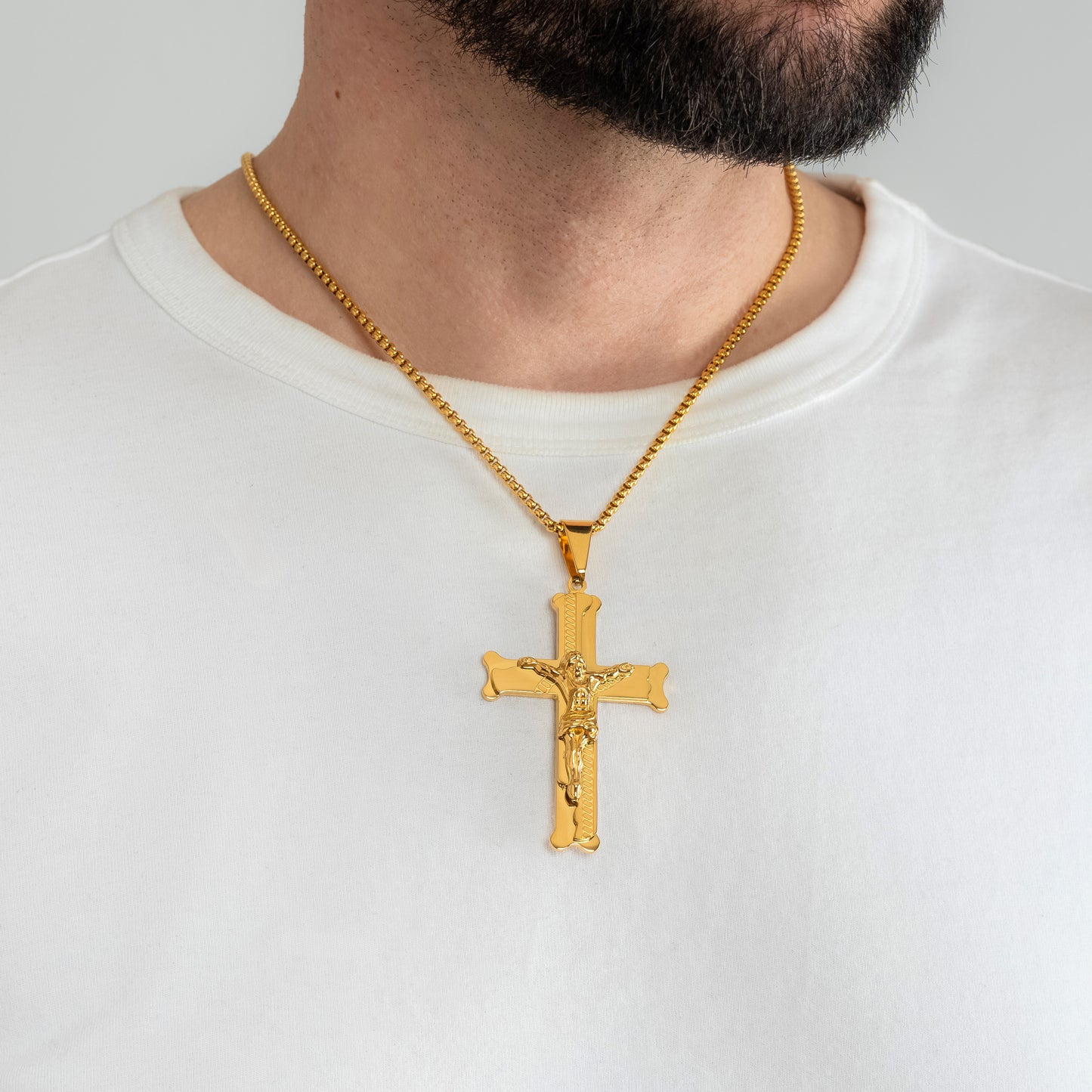 A male model in a white t-shirt wearing a Bliss Crucifix Cross Gold Pendant with a 3mm Gold Rope chain 22 inches. Close-up image of the non-tarnish, waterproof trending religious men's necklace.