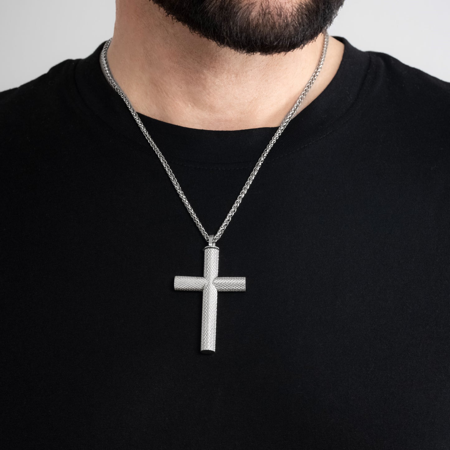 A male model in a black t-shirt wearing a Bison Cross Silver Self-fill Pendant with a 3mm Silver Spiga chain 22 inches. Close-up image of the non-tarnish trending religious men's necklace.