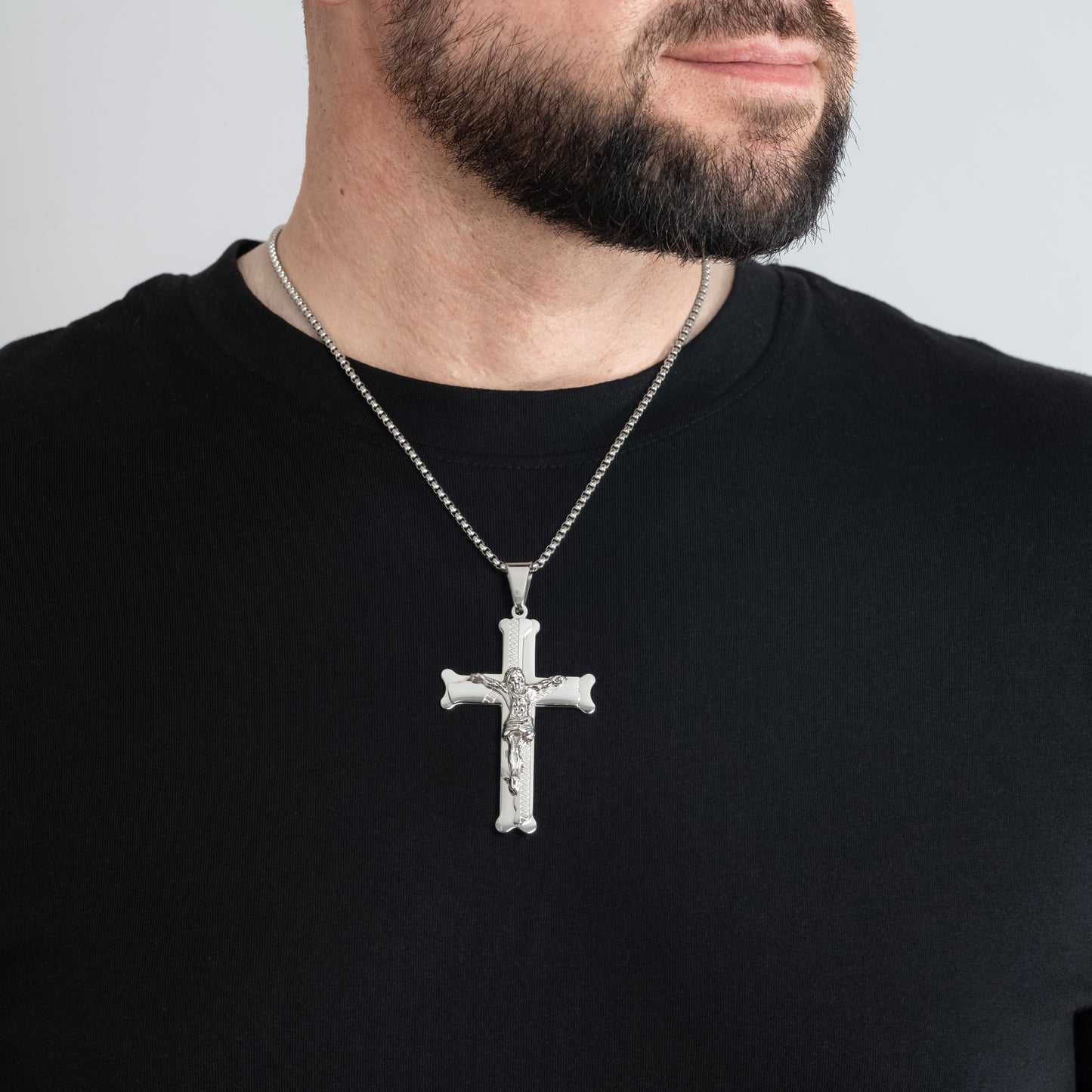 A male model in a black t-shirt wearing a Bliss Crucifix Cross Gold Pendant with a 3mm Silver Round Box Link chain 22 inches.