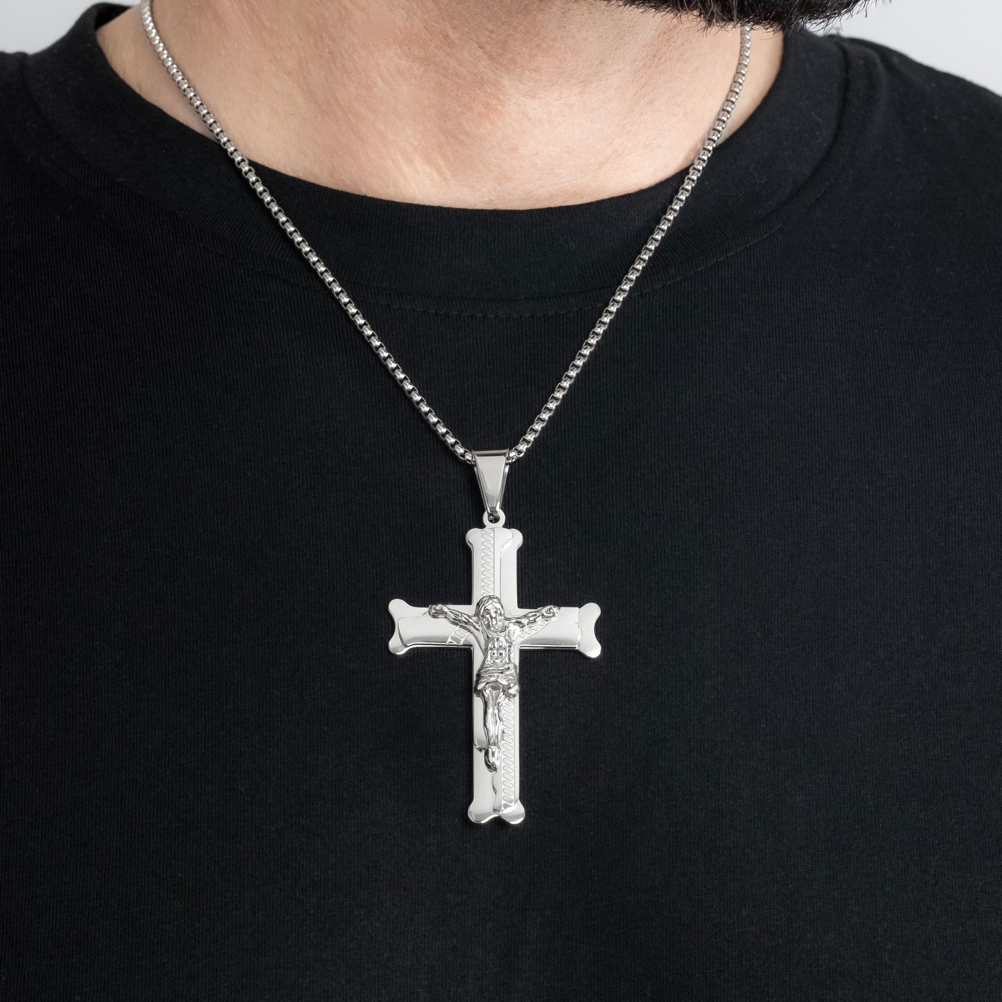 A male model in a black t-shirt wearing a Bliss Crucifix Cross Silver Pendant with a 3mm Silver Round Box Link chain 22 inches. Close-up image of the non-tarnish, waterproof trending men's jewellery.