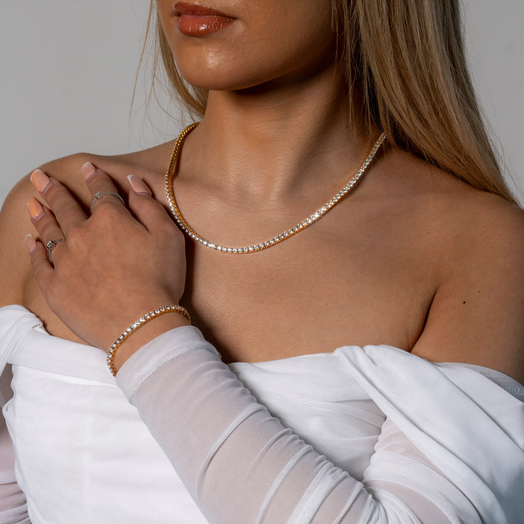 Female model in white dress wearing Cubic Zirconia 3mm Gold Tennis Necklace and Bracelet set