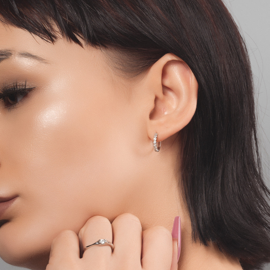 Female model wearing huggie hoop silver earrings with cubic zirconia