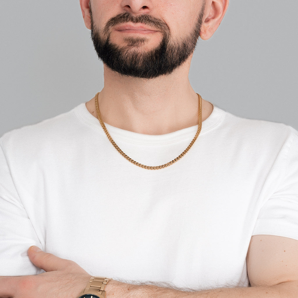 A bearded brutal man in white t-shirt wearing Gold Miami Cuban Chain 5 mm, 22 inches with gold watch to match the accessories to highlight the outfit.
