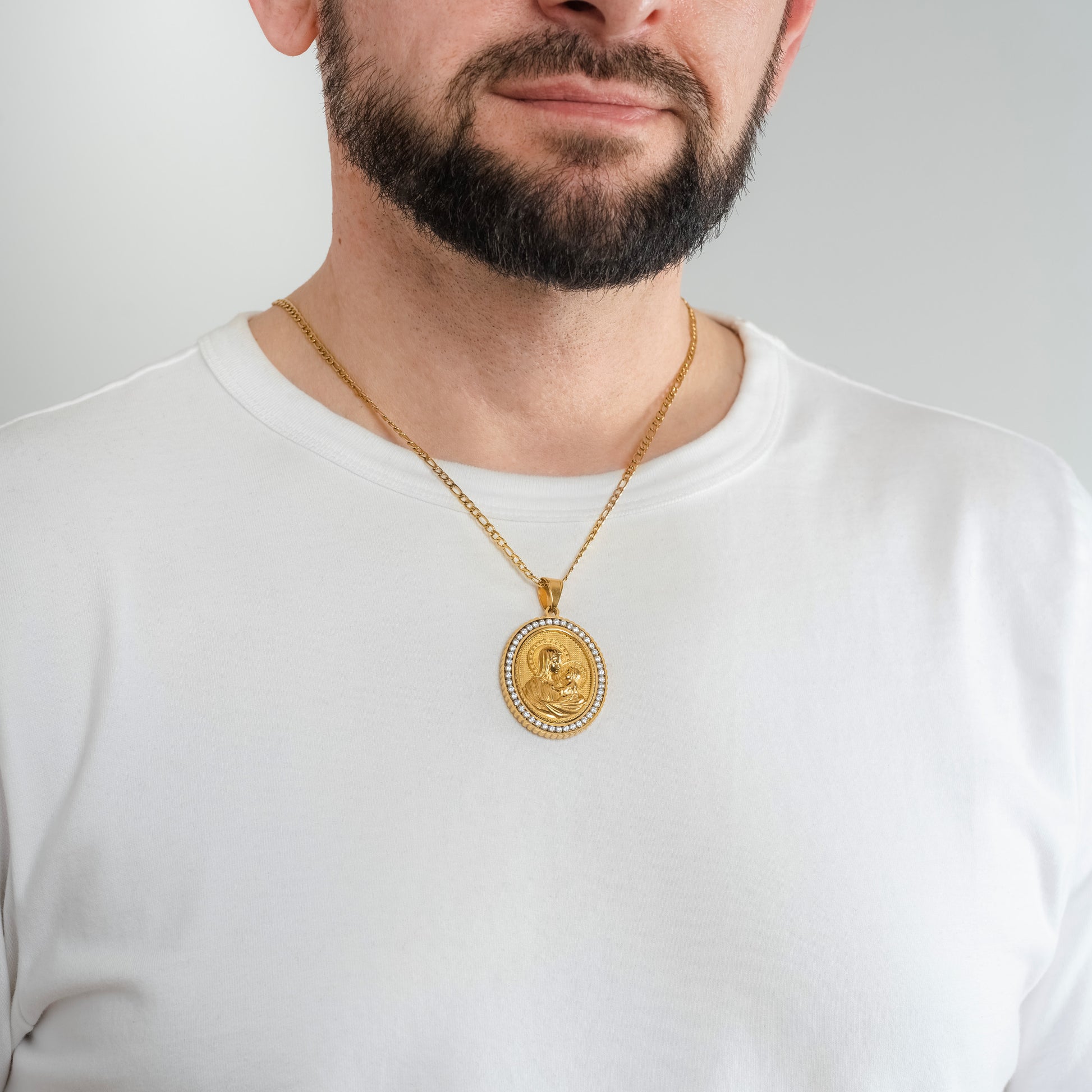 A male model in a white t-shirt wearing a Mary, Mother of Jesus Gold Pendant with a 3mm Figaro Gold chain 22 inches.