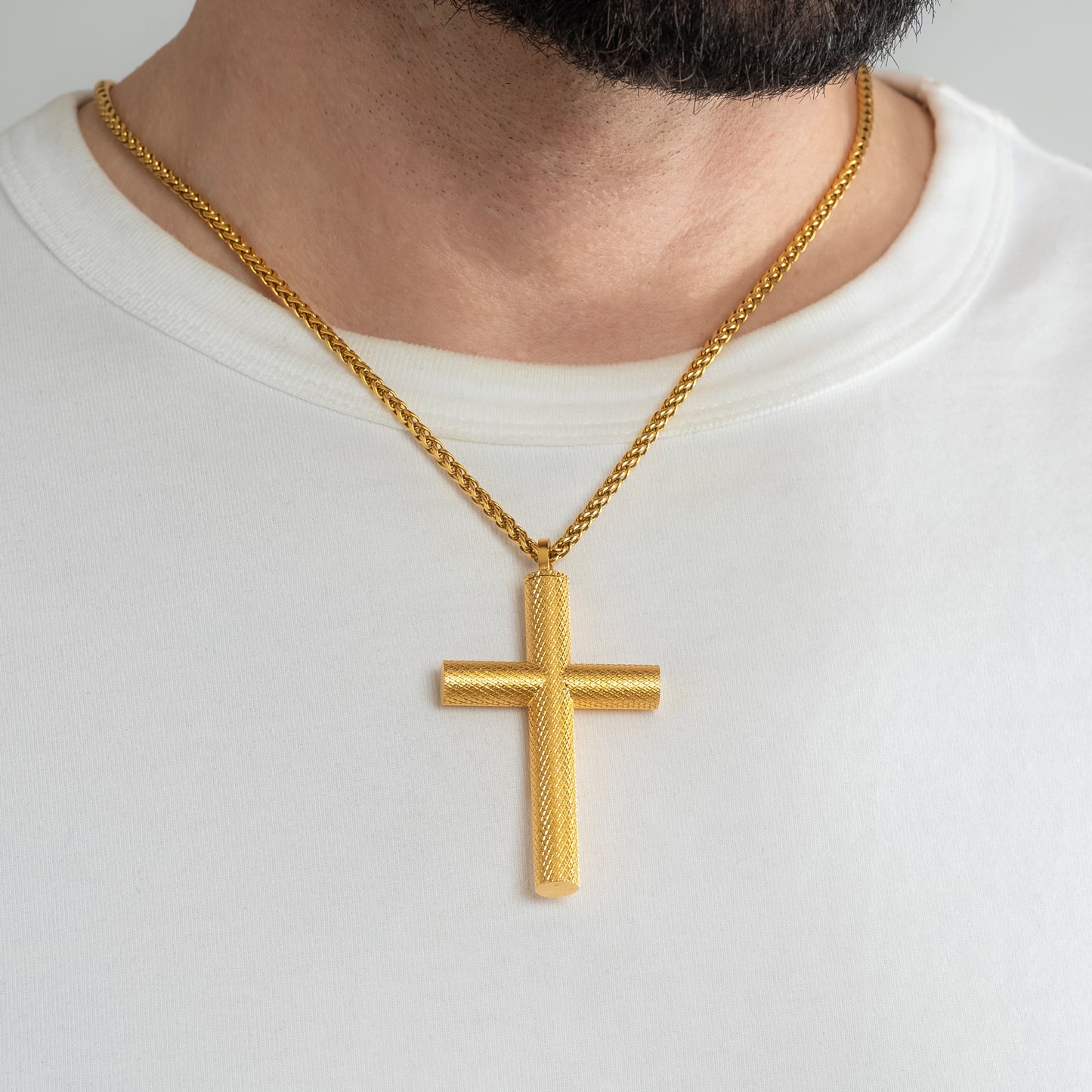 A male model in a white t-shirt wearing a Bison Cross Gold Self-fill Pendant with a 3mm Gold Spiga chain 22 inches. Close-up image of the non-tarnish trending religious men's necklace.