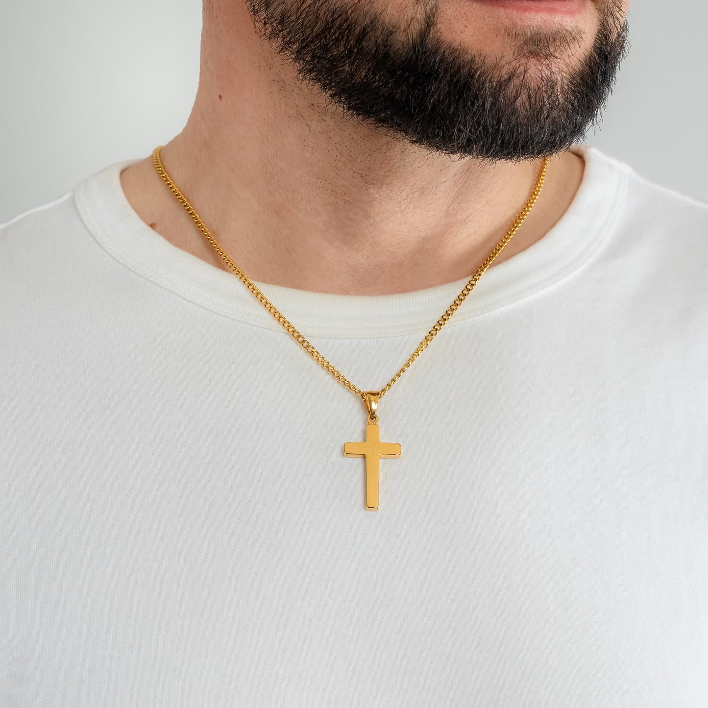 A male model in a white t-shirt wearing a Classic Cross Gold Pendant with a 3mm Micro Cuban Gold chain 22 inches. Close-up image of the waterproof, tarnish-free trending men's religious necklace.