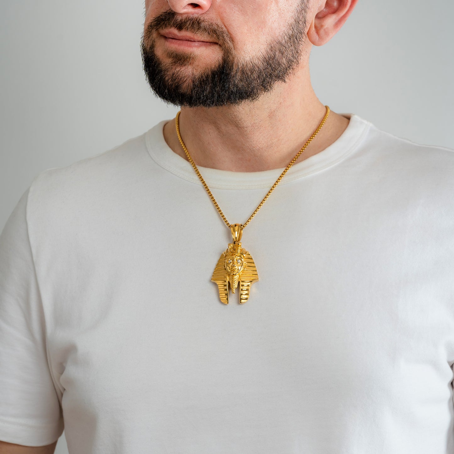 A male model in a white t-shirt wearing a Pharaoh Tutankhamun Gold Pendant with a 3mm Round Box link Gold chain 22 inches.