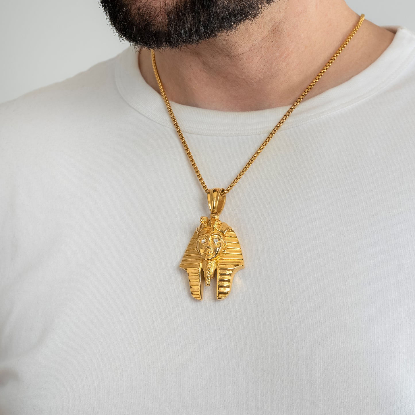 A male model in a white t-shirt wearing a Pharaoh Tutankhamun Gold Pendant with a 3mm Round Box link Gold chain 22 inches. Close-up image of the waterproof, tarnish-free, powerful and meaningful men's necklace talisman.