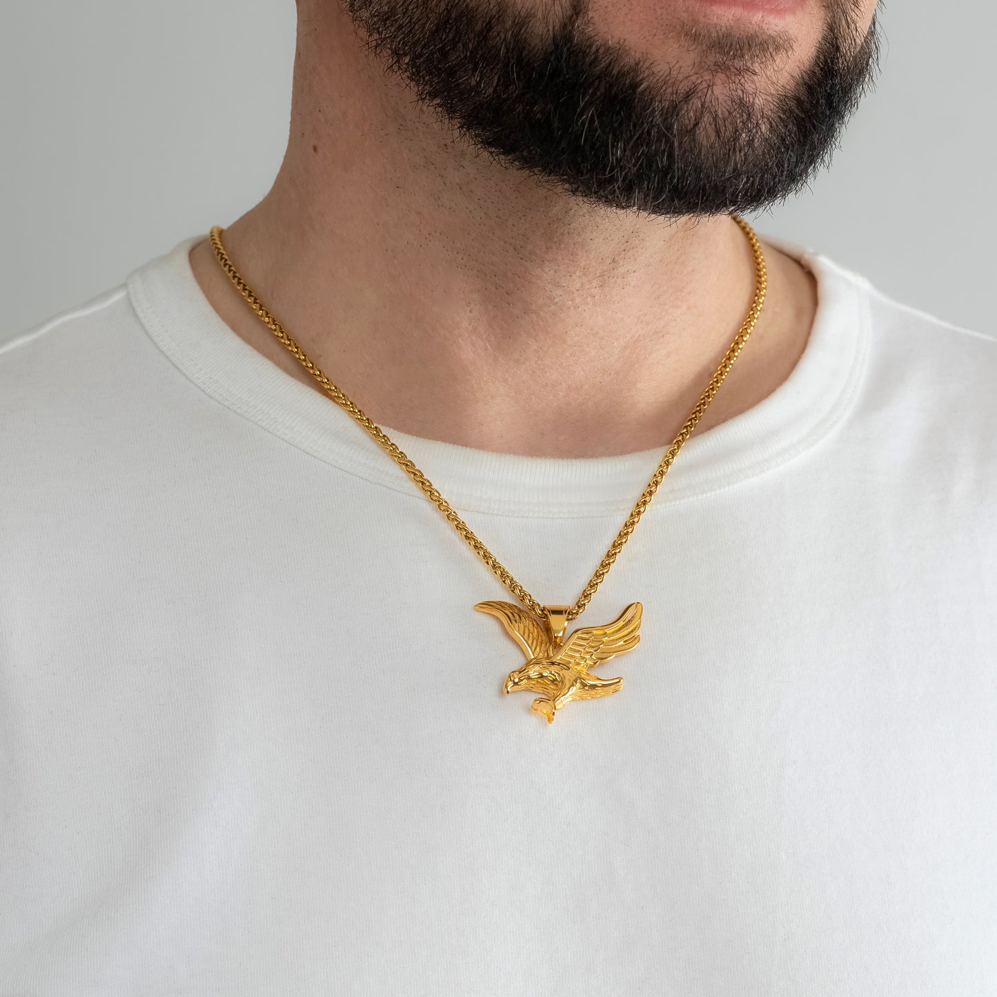 A male model in a white t-shirt wearing a Eagle Gold Pendant with a 3mm Spiga (Wheat) Gold chain 22 inches. Close-up image of the tarnish-free, sweatproof and waterproof powerful men's necklace.