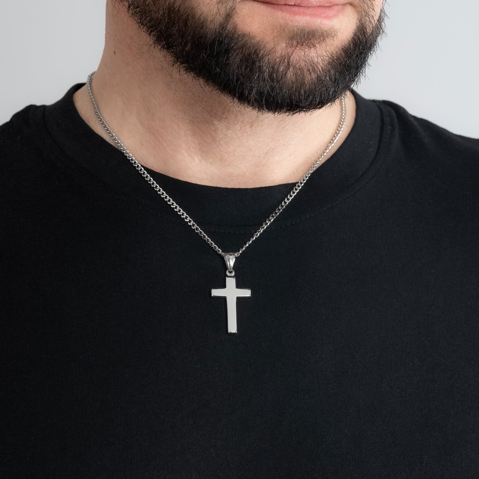 A male model in a black t-shirt wearing a Classic Cross Silver Pendant with a 3mm Silver Micro Cuban chain 22 inches. Close-up image of the waterproof, tarnish-free trending men's necklace.