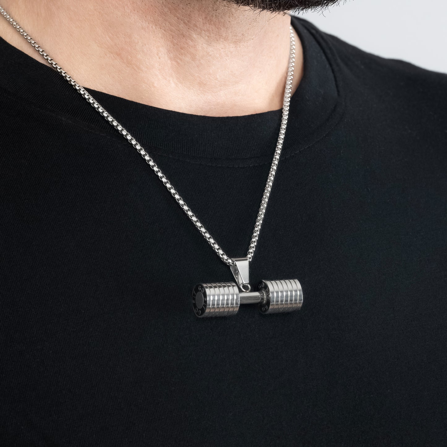 A male model in a black t-shirt wearing a Dumbbell Fitness Silver Pendant with a 3mm Round Box link Silver chain 22 inches. Close-up image of the tarnish-free, sweatproof and waterproof motivational men's necklace.