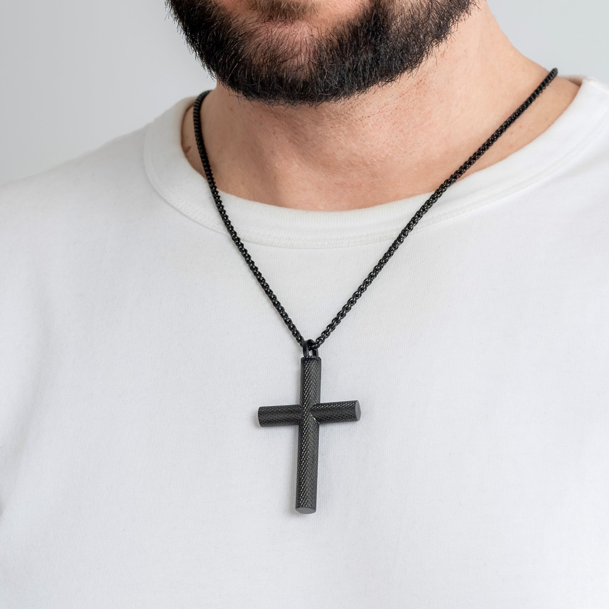 A male model in a white t-shirt wearing a Bison Cross Black Self-fill Pendant with a 3mm Black Spiga chain 24 inches. Close-up image of the non-tarnish trending men's religious necklace.