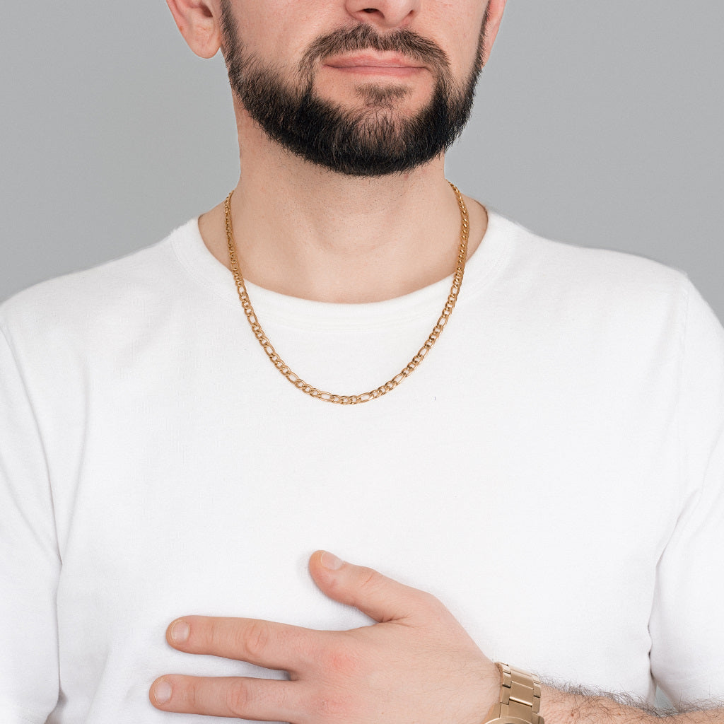 A bearded male model in white t-shirt wearing Gold Figaro Link Chain 5 mm, 22 inches with Gold watch to perfectly match the accessories to highlight the look.