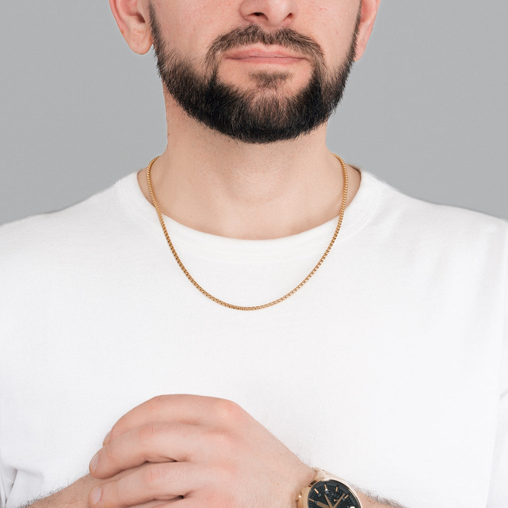 A bearded male model in white t-shirt wearing Gold Round Box link Chain 3mm, 22 inches, and gold watch to colour match the accessories