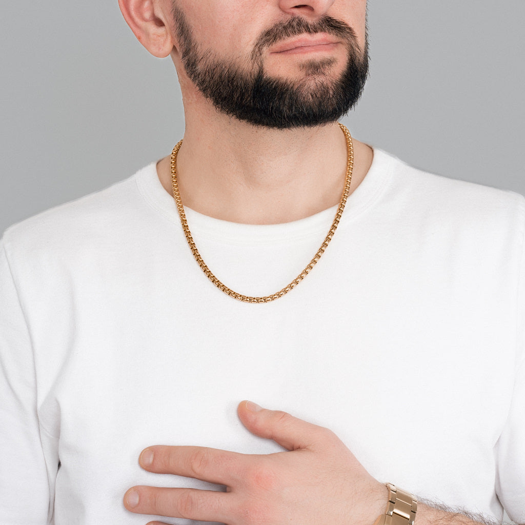A bearded male model in white t-shirt wearing Gold Round Box Link Chain 5 mm, 22 inches with gold watch to match the accessories.